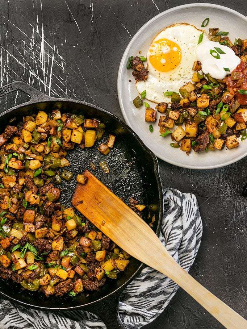 A cast iron skillet full of Chorizo Breakfast Hash next to a serving plate with a sunny side up egg