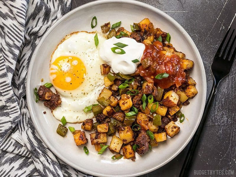 Chorizo Breakfast Hash on a plate with a sunny side up egg, sour cream, and salsa