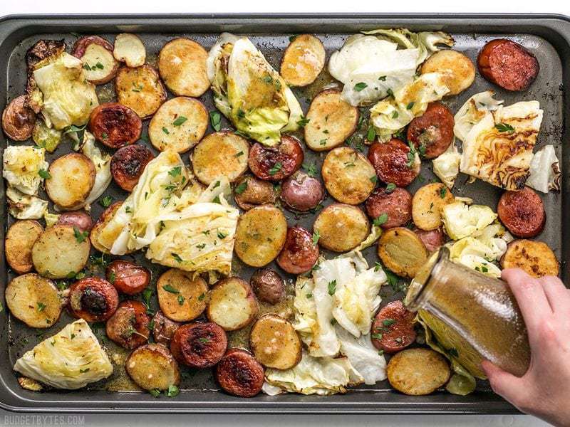 Homemade Mustard Vinaigrette being drizzled over roasted kielbasa, potatoes, and cabbage