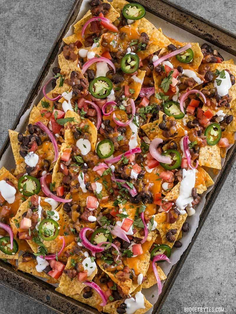 Overhead view of a baking sheet full of baked black bean nachos topped with pickled red onions, jalapeño, and sour cream