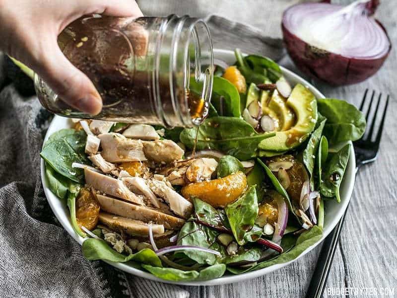 Sesame dressing being poured from a mason jar onto Chicken and Mandarin Salad 