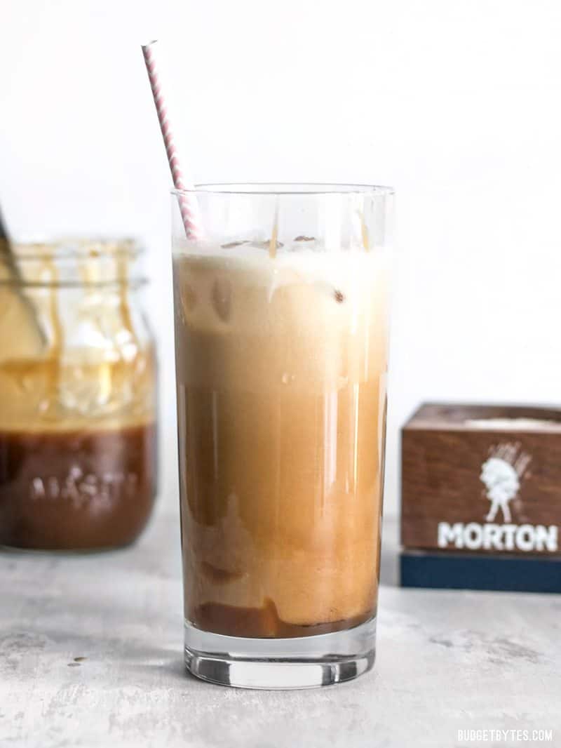 Homemade Salted Caramel Iced Coffee viewed from the side with a jar full of caramel and a salt conter in the background