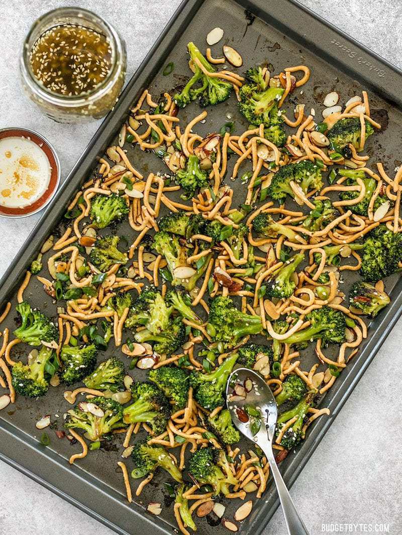 A sheet pan full of Roasted Broccoli Salad with Almonds and a jar of Simple Sesame Dressing on the side