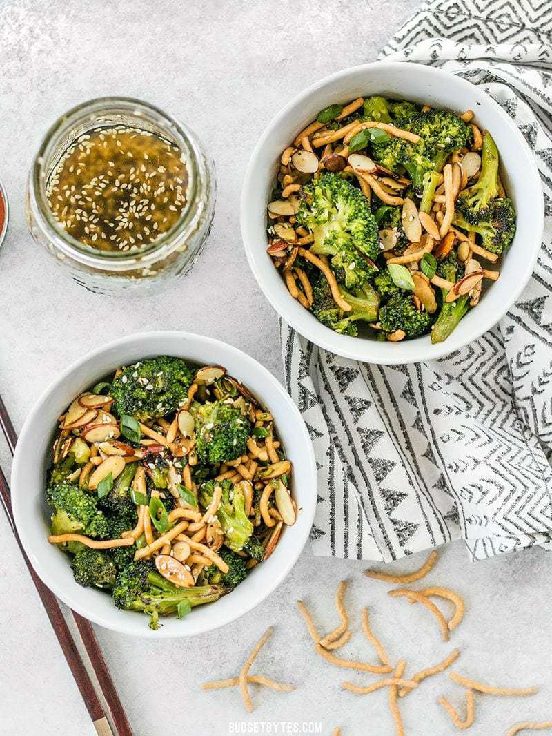 Two bowls of Roasted Broccoli Salad with Almonds with a jar of Simple Sesame Dressing on the side