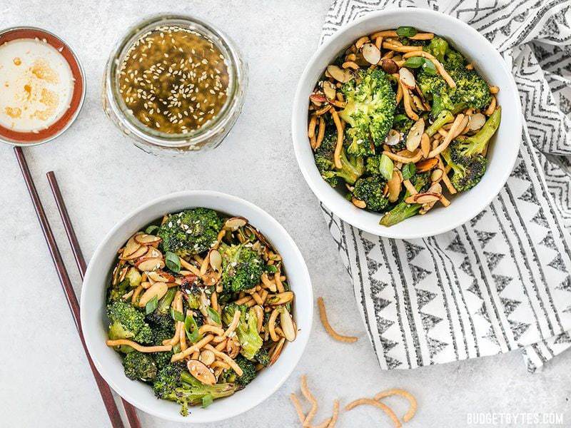 Two bowls of Roasted Broccoli Salad with Almonds with a jar of simple sesame dressing and a pair of chopsticks