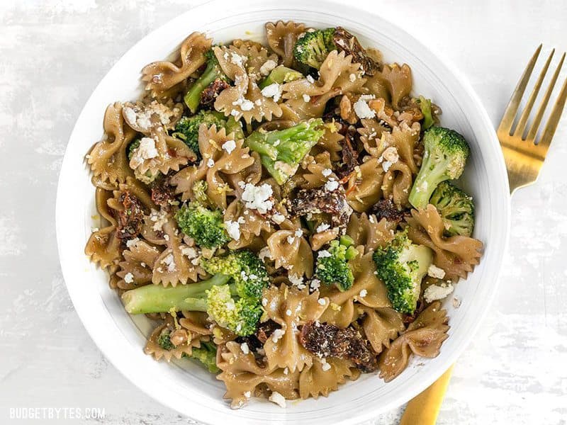 Finished Skillet Pasta with Sun Dried Tomatoes Walnuts and Feta in a white bowl with a gold fork