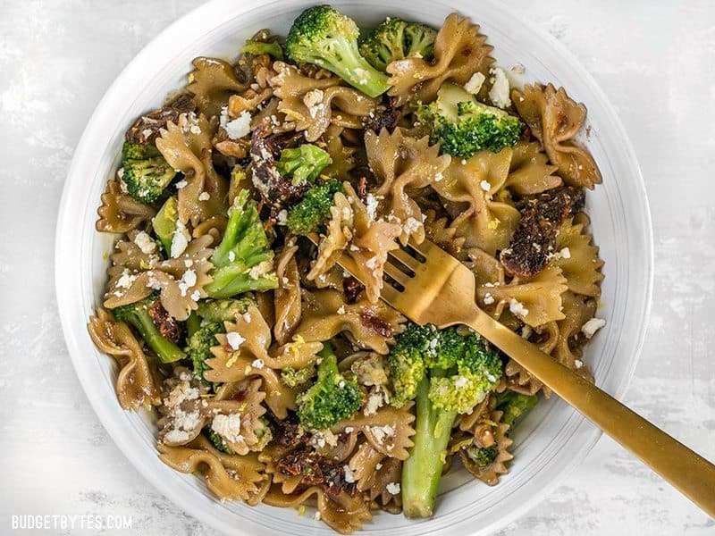 A bowl of Skillet Pasta with Sun Dried Tomatoes Walnuts and Feta with a gold fork