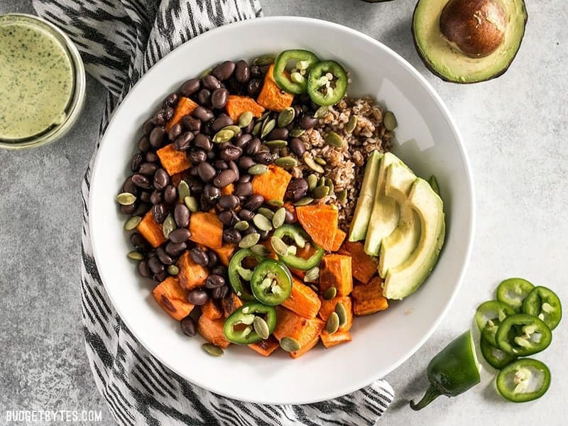 A Sweet Potato Grain Bowl with green tahini sauce, avocado, and jalapeno on the side.