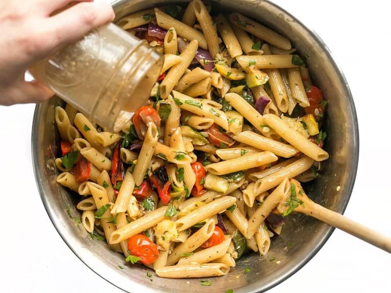 Balsamic vinaigrette being poured onto Grilled Vegetable Pasta Salad from a mason jar