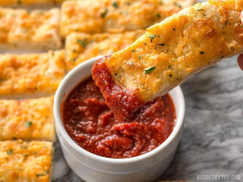 One piece of Homemade Cheesy Garlic Bread being dipped into pizza sauce