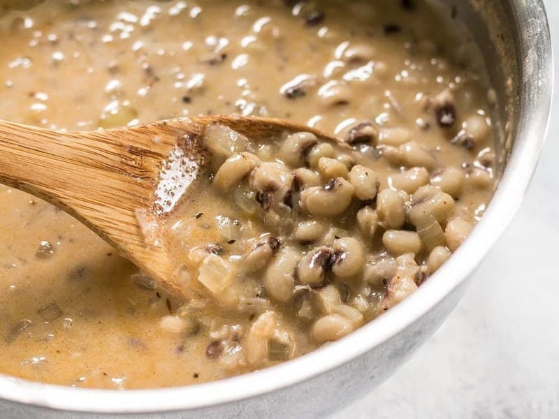 Close up of cooked Coconut Jerk Peas in the sauce pot being lifted by a wooden spoon