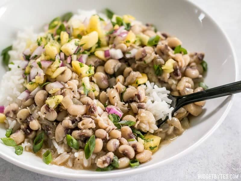 Close up side view of a bowl of Coconut Jerk Peas with rice and pineapple salsa