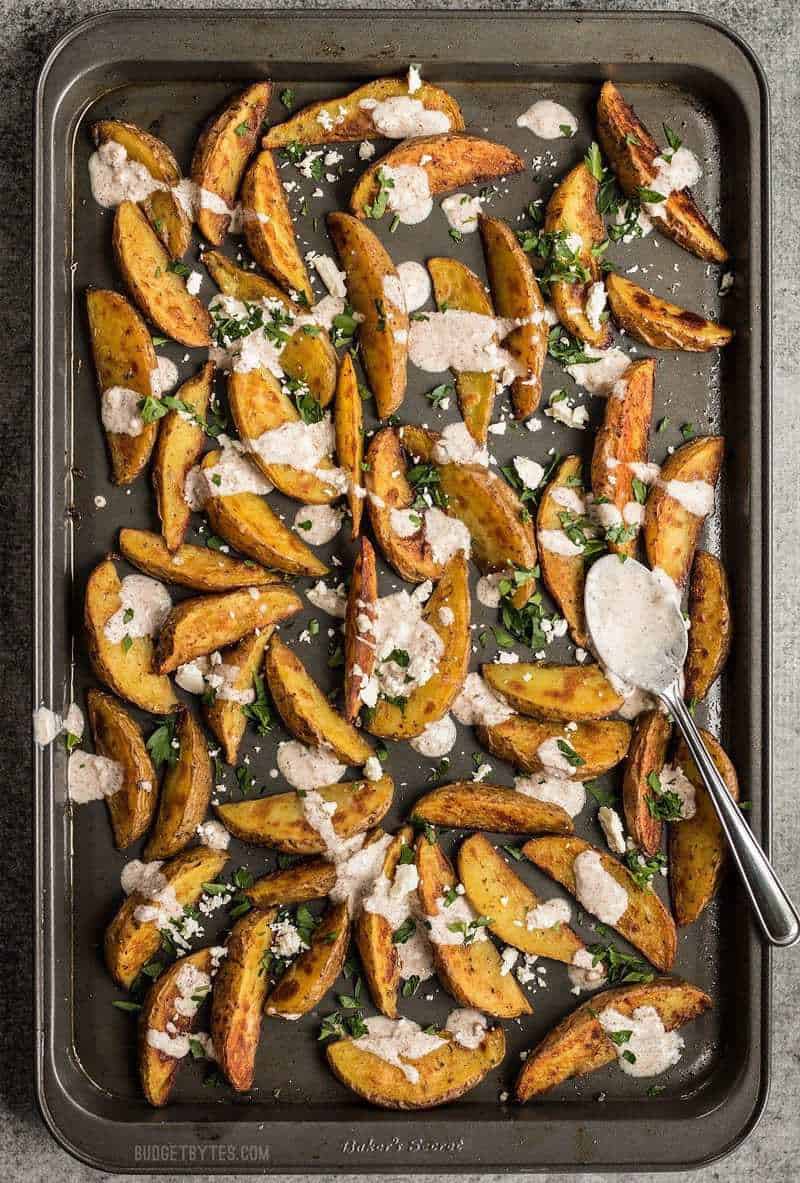 Roasted Potato Wedges with shawarma sauce on the baking sheet with a spoon full of shawarma sauce