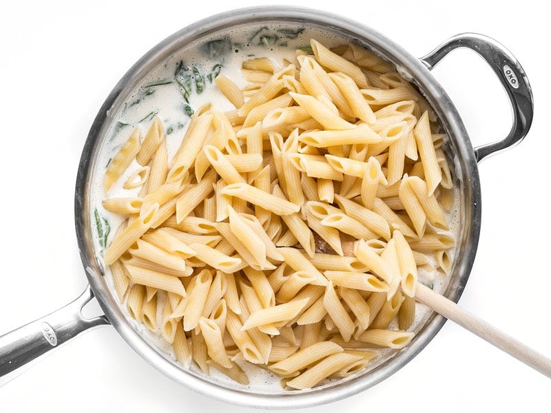 Cooked pasta added to spinach alfredo sauce in the skillet