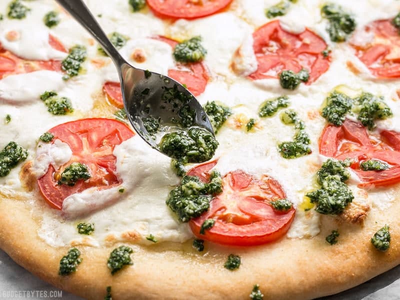 Parsley pesto being drizzled onto a freshly baked white pizza