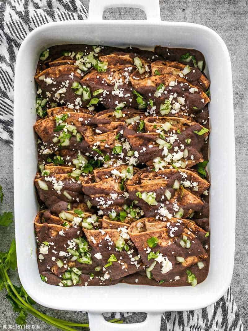 A baking dish full of folded Enfrijoladas garnished with onion and cheese