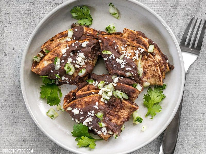 Enfrijoladas on a plate garnished with onion, cilantro, and cheese