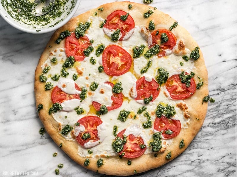 A bowl of parsley pesto next to a freshly baked white pizza