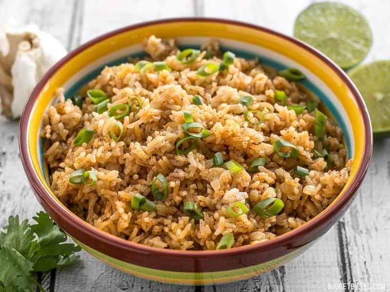 Front view of the striped bowl full of Taco Rice, garlic and limes in the back