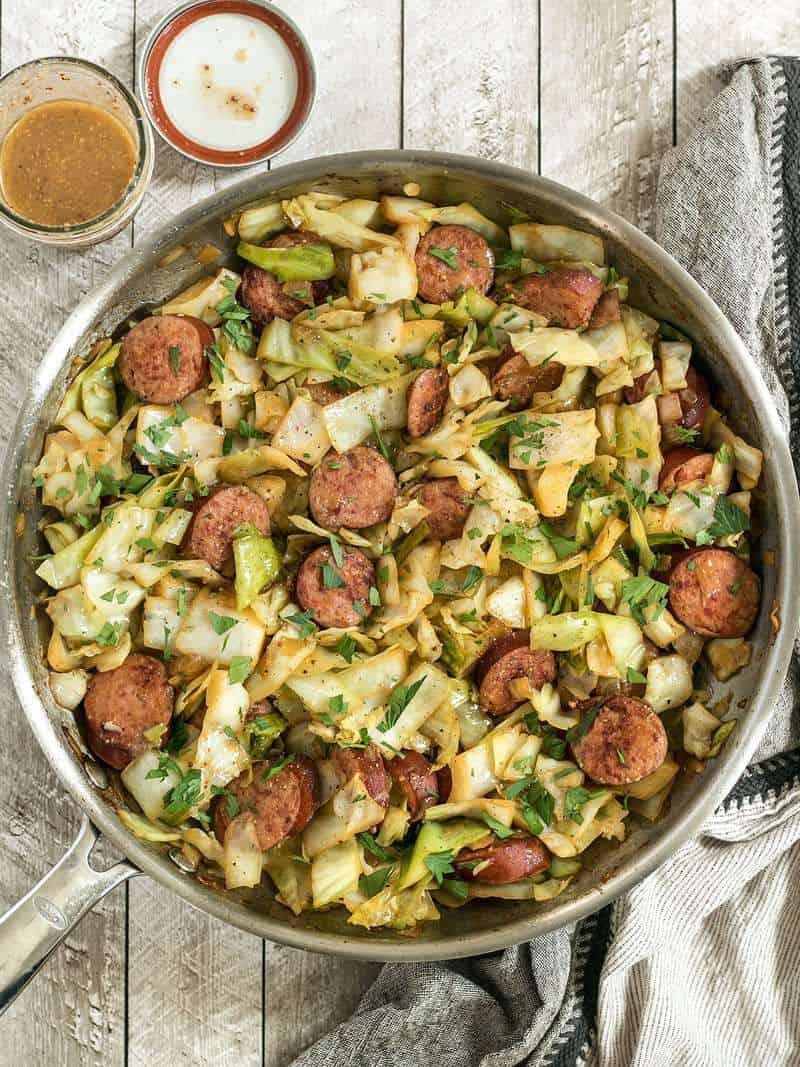 A full pan of Kielbasa and Cabbage Skillet with a jar of tangy mustard vinaigrette by its side. 