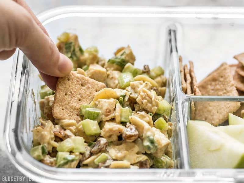 A cracker being dipped into Curry Chicken Salad in the meal prep container