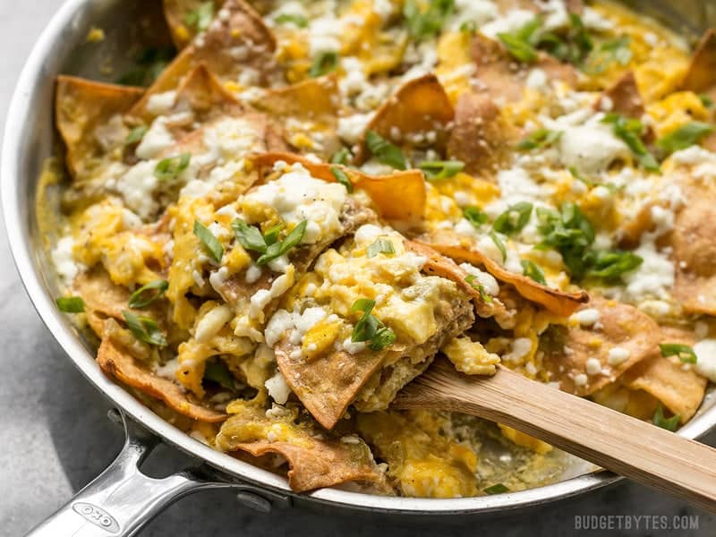 Front view of a skillet full of Green Chile Migas being scooped with a wooden spatula. 