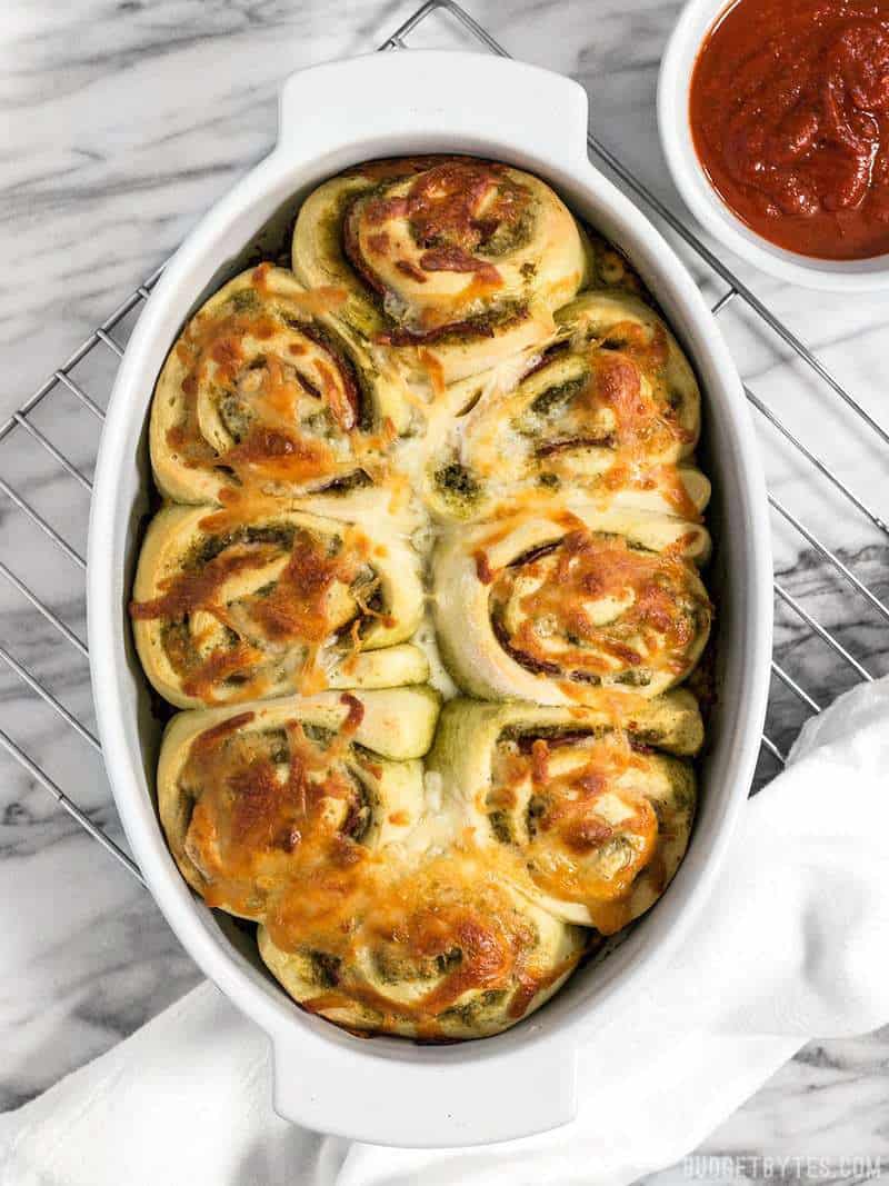 A baking dish full of Pesto Pizza Rolls on a cooling rack with pizza sauce on the side