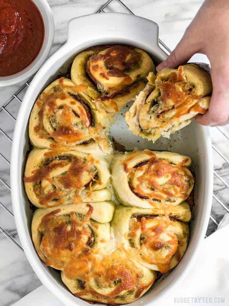 A hand taking a Pesto Pizza Roll out of the baking dish