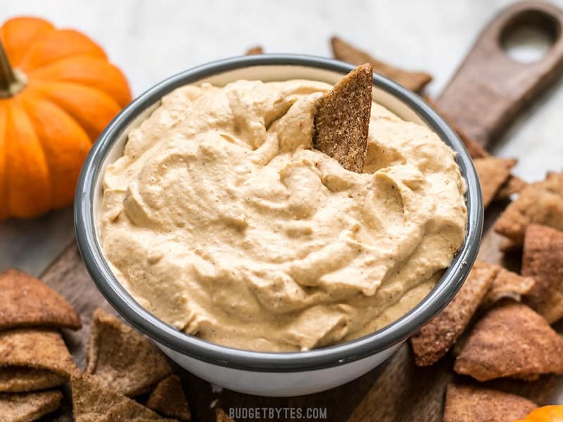 Front view of a Cinnamon Pita Crisp being dipped into a bowl of fluffy Pumpkin Cheesecake Mousse