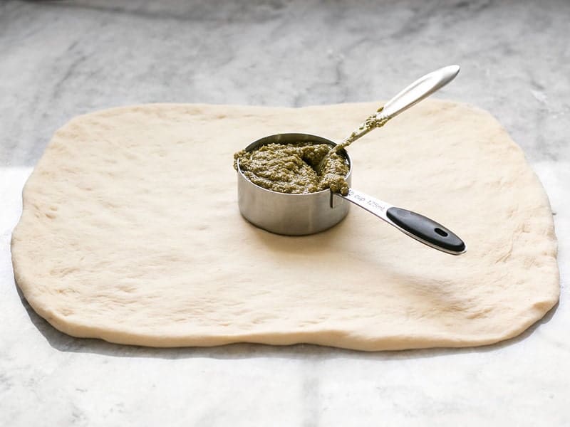 Square Pizza Dough with a measuring cup full of pesto on top