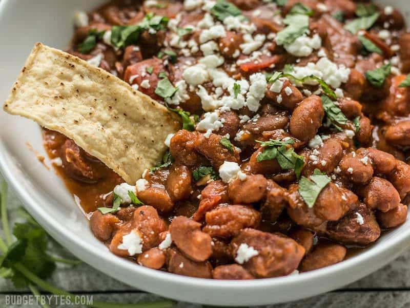 A tortilla chip being dipped into a bowl of Instant Pot Pinto Beans with Chorizo