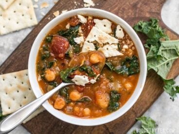 Overhead view of a bowl of Smoky Potato and Chickpea Stew with crumbled saltine crackers and a spoon in the middle