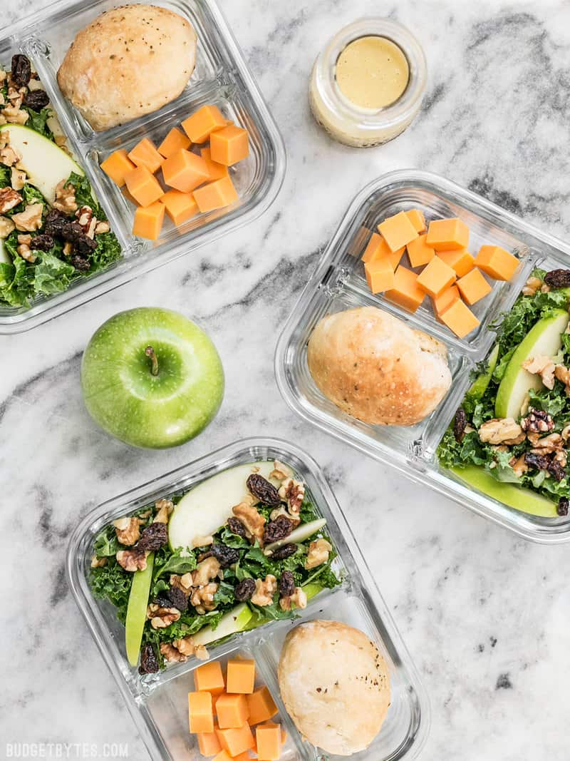 This Apple Dijon Kale Salad Meal Prep containers scattered, with an apple and dressing near by.