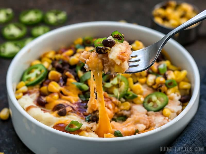 A fork digging into Loaded Mashed Potato Bowls, cheese pulling