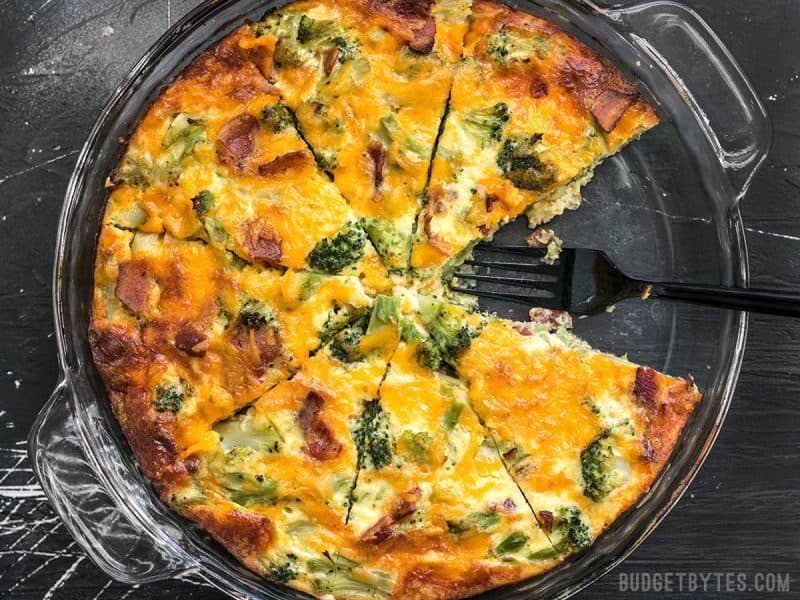 A sliced Bacon Broccoli Cheddar Crustless Quiche in a glass pie plate with one piece missing.