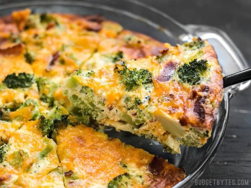 One slice of Bacon Broccoli Cheddar Crustless Quiche being lifted out of a pie plate.