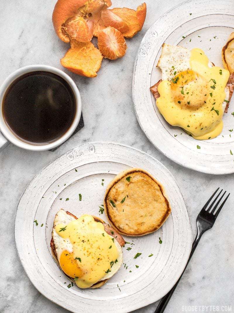 Two plates of Almost Eggs Benedict with a cup of coffee and tangerine near by