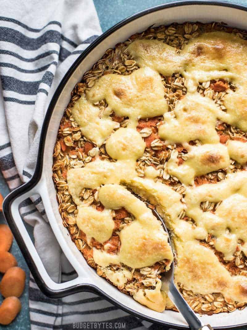 A casserole dish of Carrot Cake Baked Oatmeal with a cheesecake topping being scooped by a serving spoon