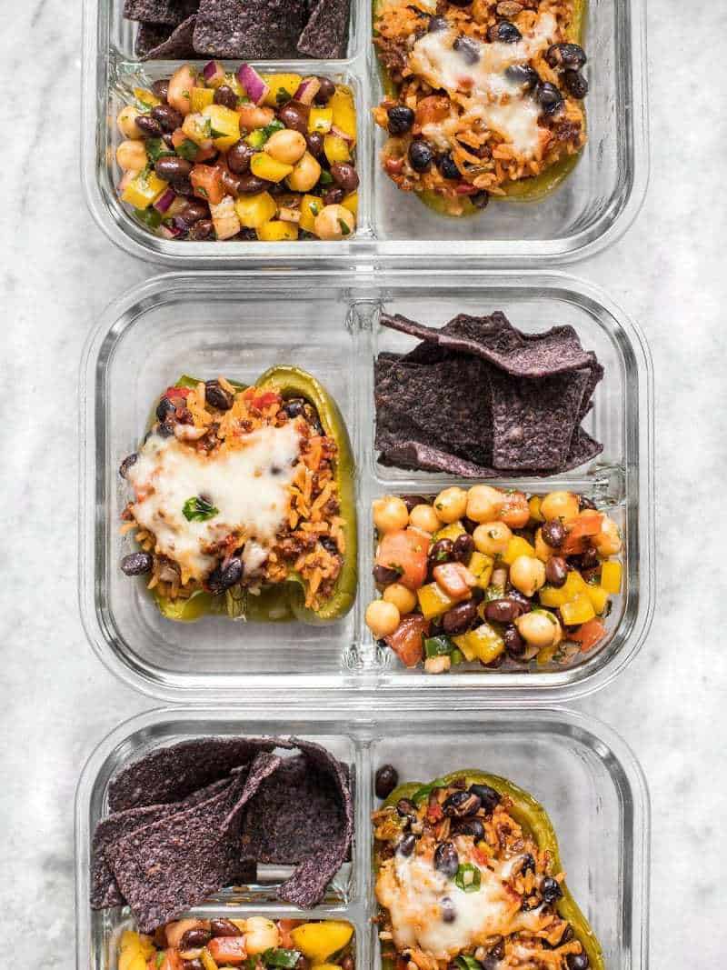 Three meal prep containers lined up with stuffed bell peppers, cowboy caviar, and tortilla chips