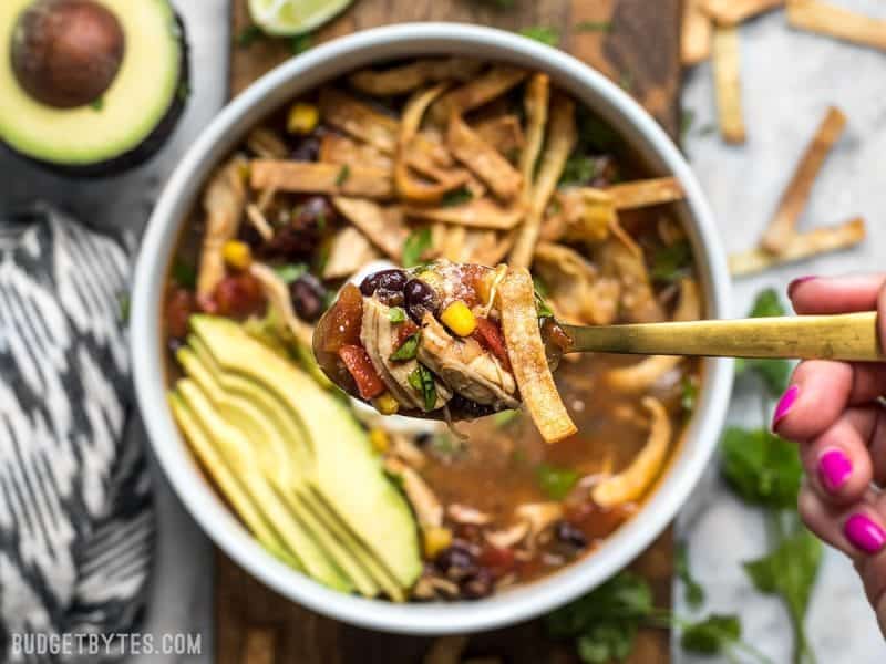 Close up of a spoonful of Slow Cooker Chicken Tortilla Soup with the bowl in the background. 