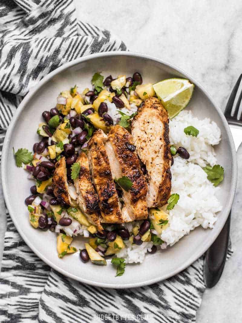 Sliced Jerk Chicken on a bed of rice with Pineapple Black Bean Salsa, limes, and cilantro