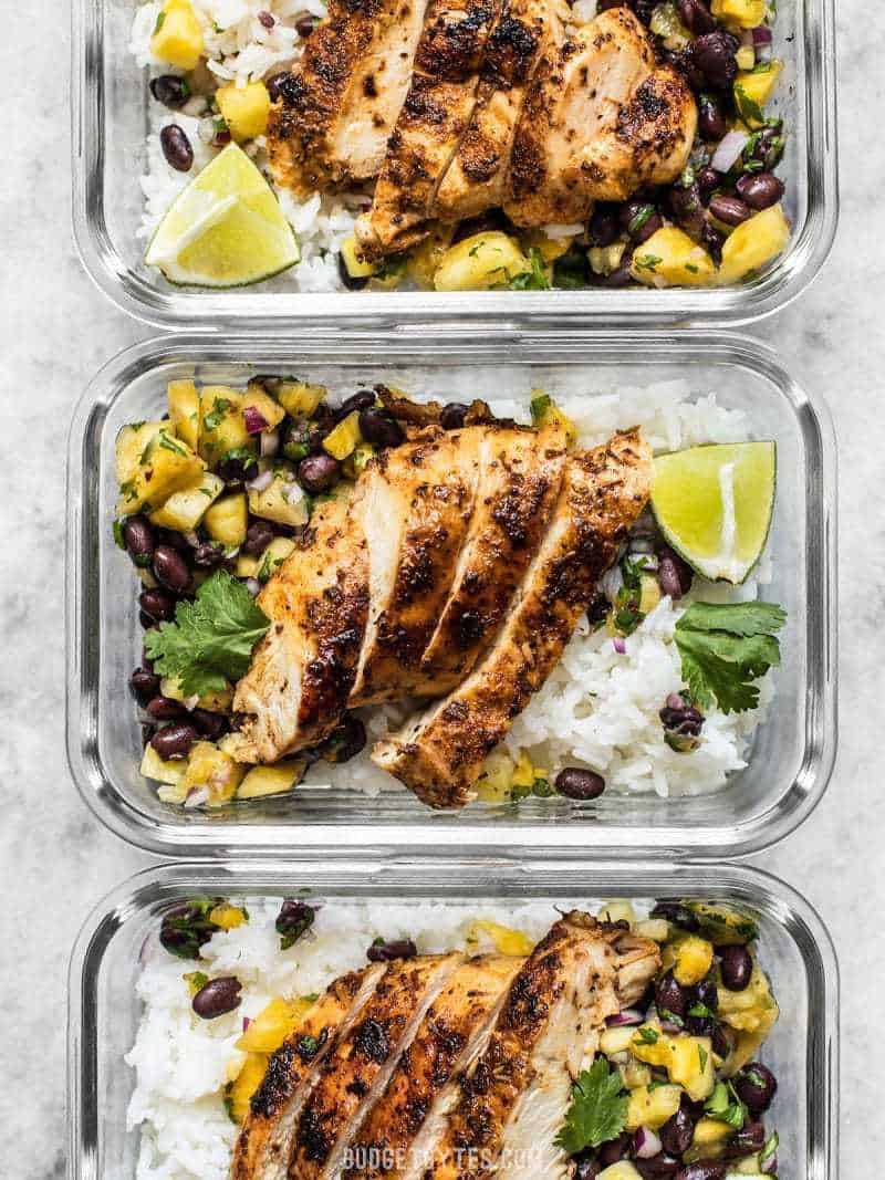 Rectangle glass meal prep containers full of Jerk Chicken with Pineapple Black Bean Salsa, rice, and limes. 