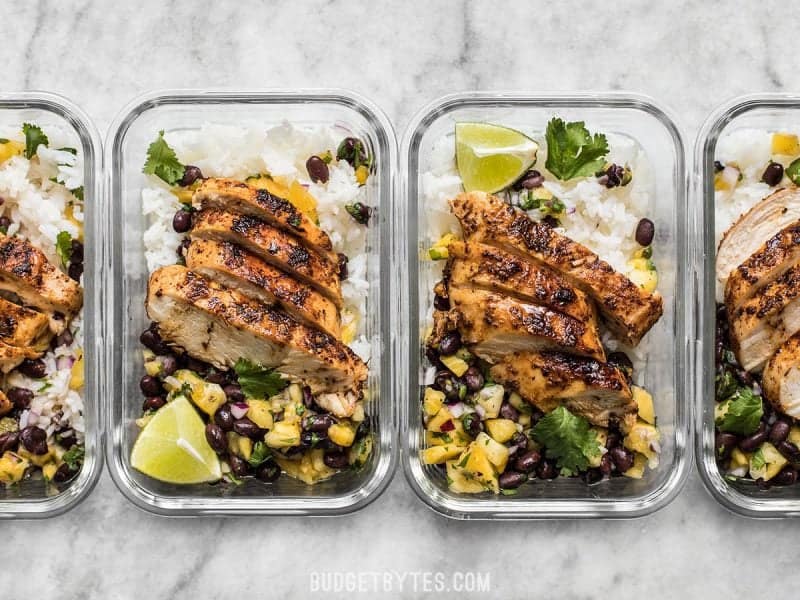 Glass meal prep containers with Jerk Chicken and Pineapple Black Bean Salsa lined up in a row.