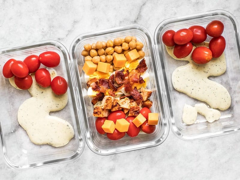 Add dressing tomatoes cheese bacon and beans to meal prep containers