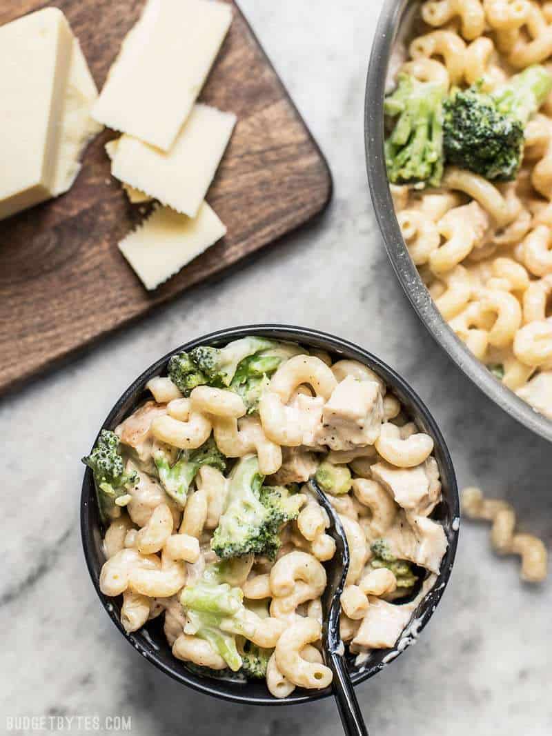 A small bowl of White Cheddar Mac and Cheese next to the skillet and sliced white cheddar