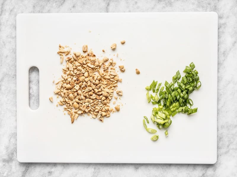 Chopped Peanuts and Sliced Green Onion on a cutting board