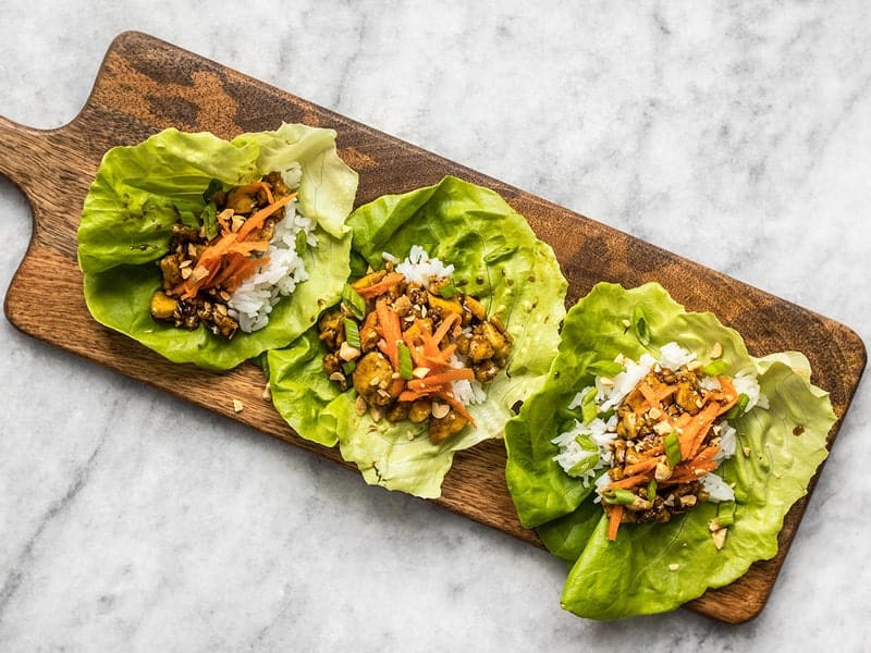 Hoisin Tofu added to lettuce cups with shredded carrot peanuts and green onion