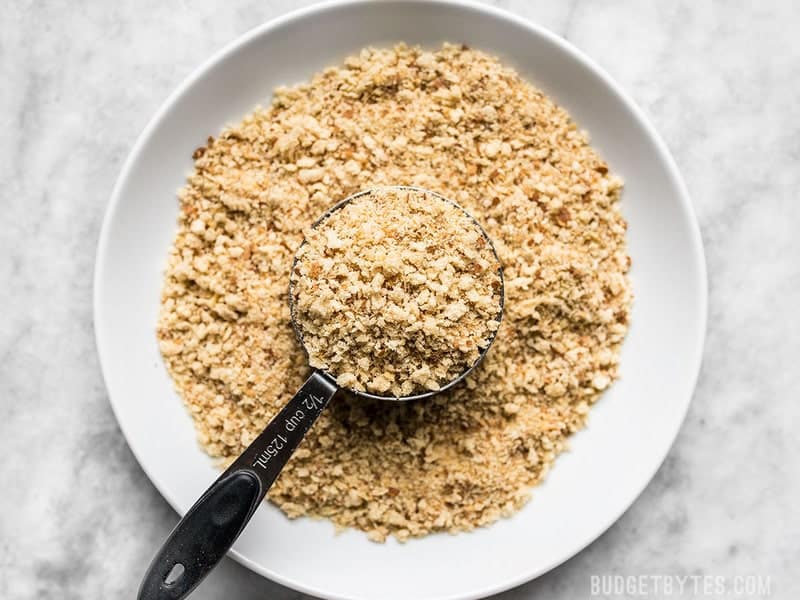 Breadcrumbs in a bowl with a measuring cup scooping some