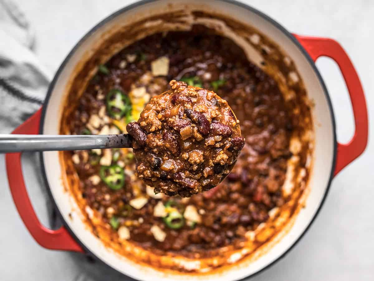 A ladle full of chili held over the pot.