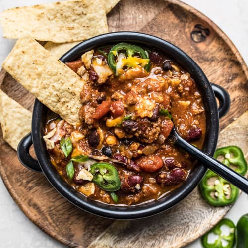 Overhead view of a bowl full of chili with toppings and a spoon in the center.